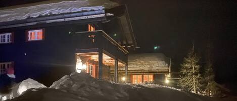 A two-story building with a snow-covered roof and a lit entrance.