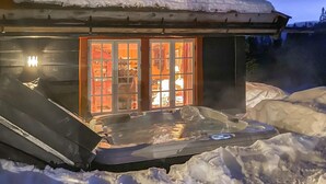 Ein schneebedecktes Gebäude mit Whirlpool und Glastür zu einem Zimmer mit sichtbaren Möbeln.