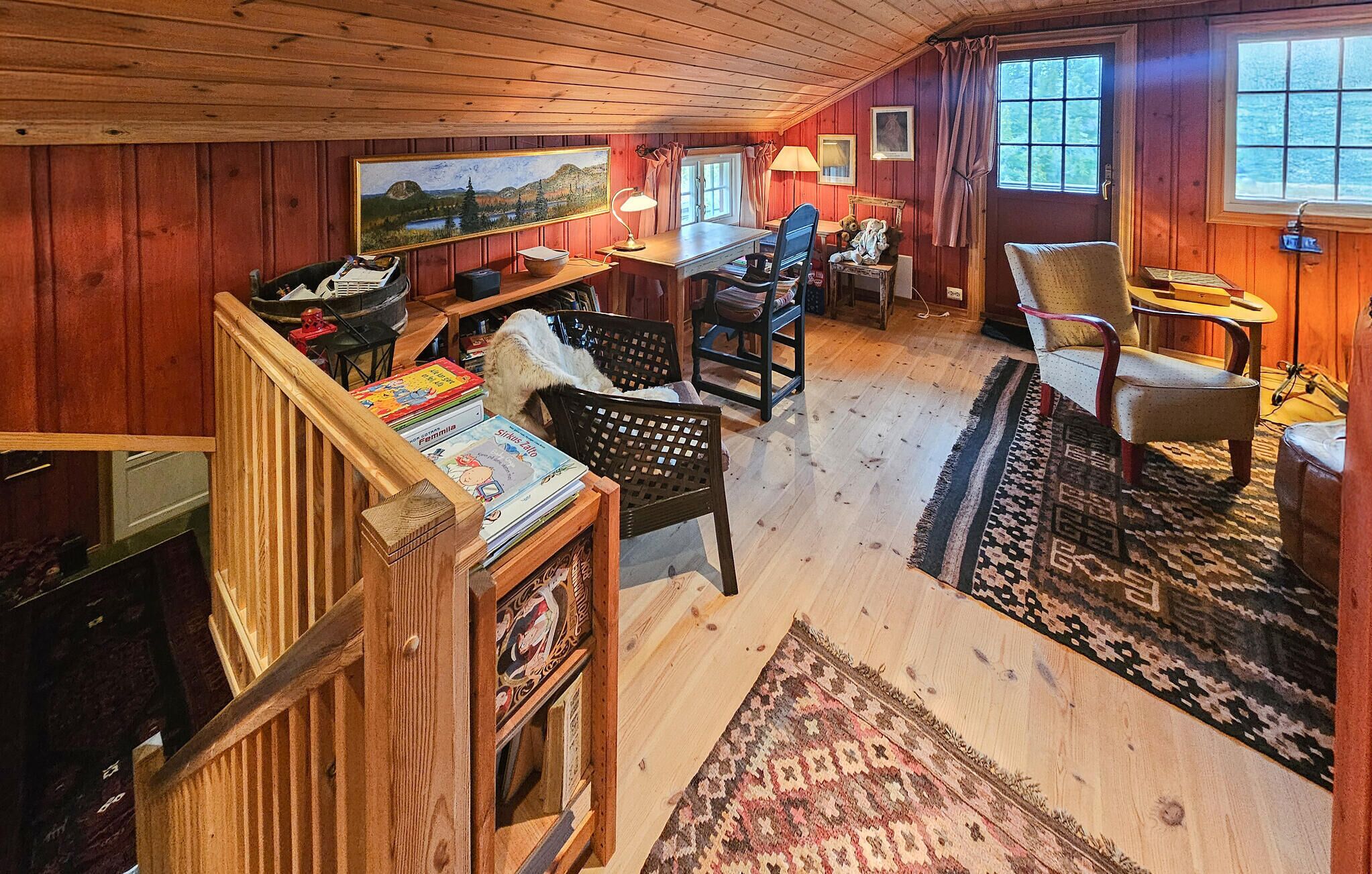 Interior acogedor de una cabaña con paredes y pisos de madera, un comedor con mesa y sillas, y una estantería llena de libros.