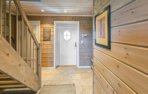 A wooden interior hallway with a staircase, a door with a geometric pattern, and a framed picture on the wall.