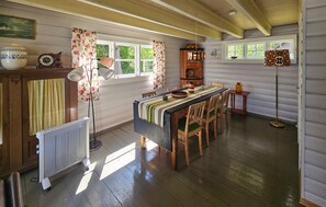 A rustic kitchen with wooden floors, a central island with chairs, a radiator, and a window with curtains.