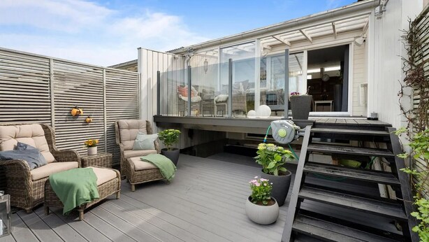 A covered outdoor deck with wicker furniture, potted plants, and a glass enclosure.