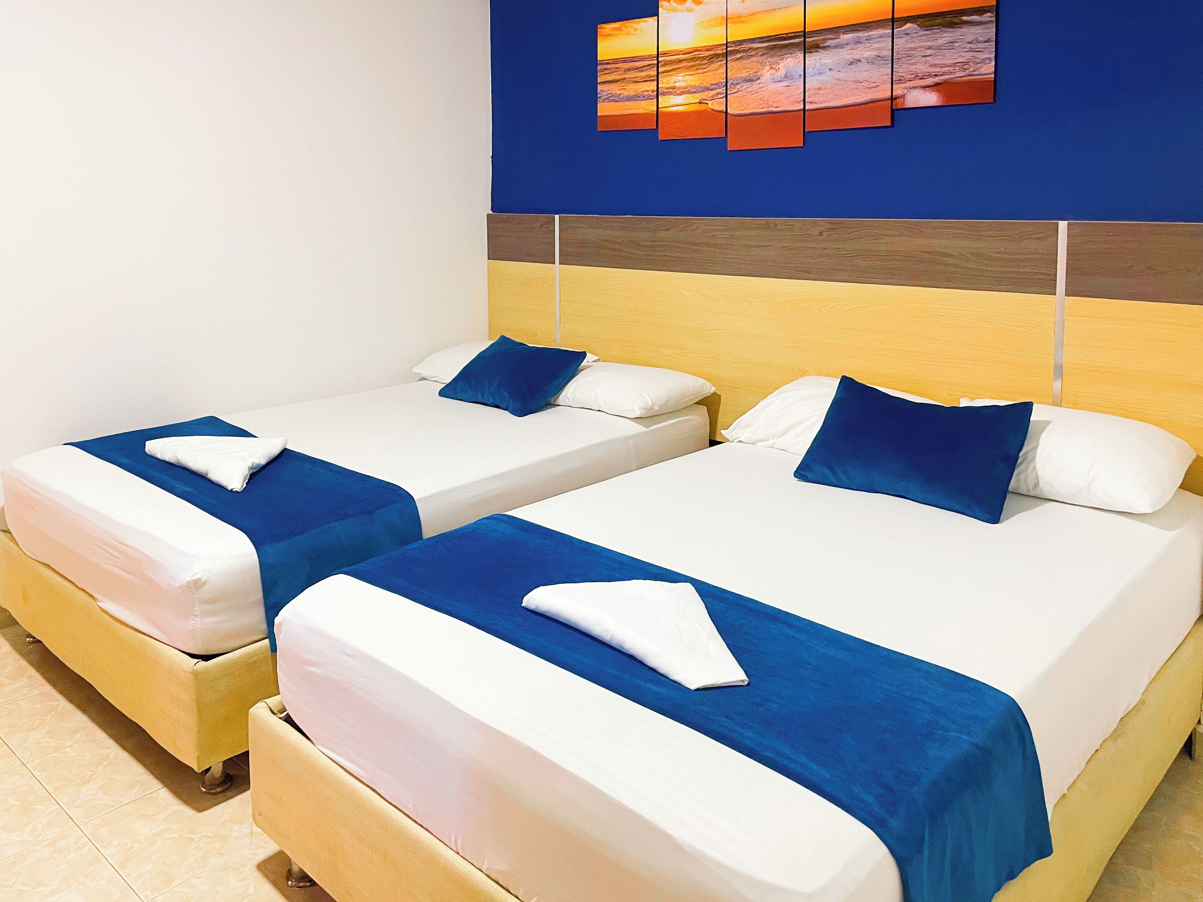 Two twin beds with blue and white bedding, a wooden headboard, and a wall art depicting a sunset over the ocean.