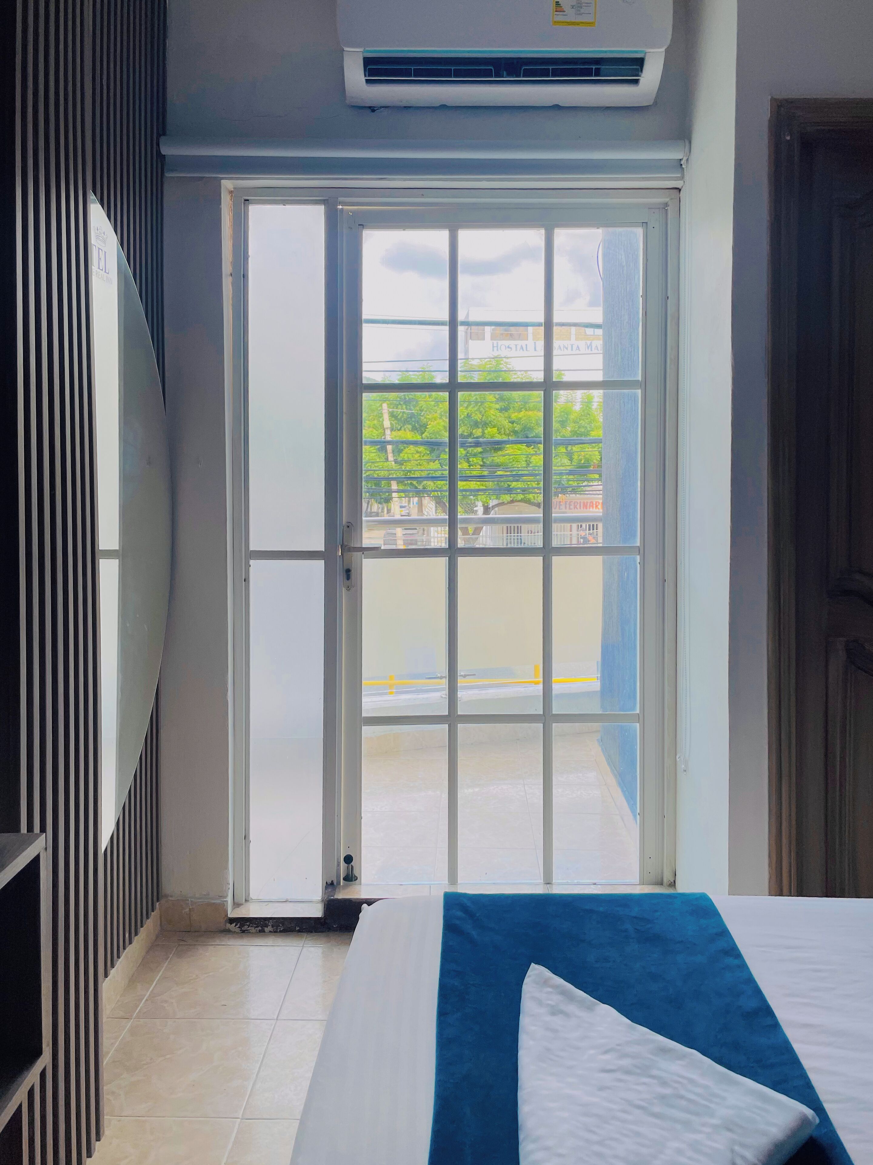 A hotel room with a bed, a window with a view of the outside, and an air conditioning unit above the window.