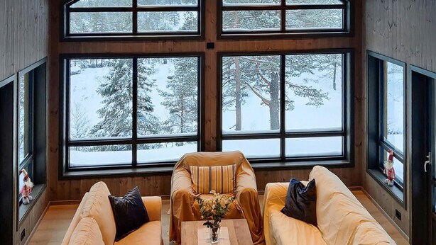 Quarto aconchegante com grandes janelas e vista para uma floresta coberta de neve.