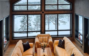 A cozy room with large windows offering a snowy forest view.