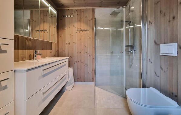 A modern bathroom with a wooden interior, a glass shower enclosure, a white sink, and a bathtub.