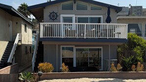 A two-story beachfront property with a balcony, a ship's wheel decoration, and a sandy beach in front. - Cozy Beachfront Getaway! (Los Angeles)