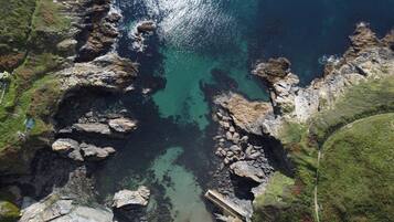 An aerial view of a coastal area with rocky terrain, clear water, and a paved path.