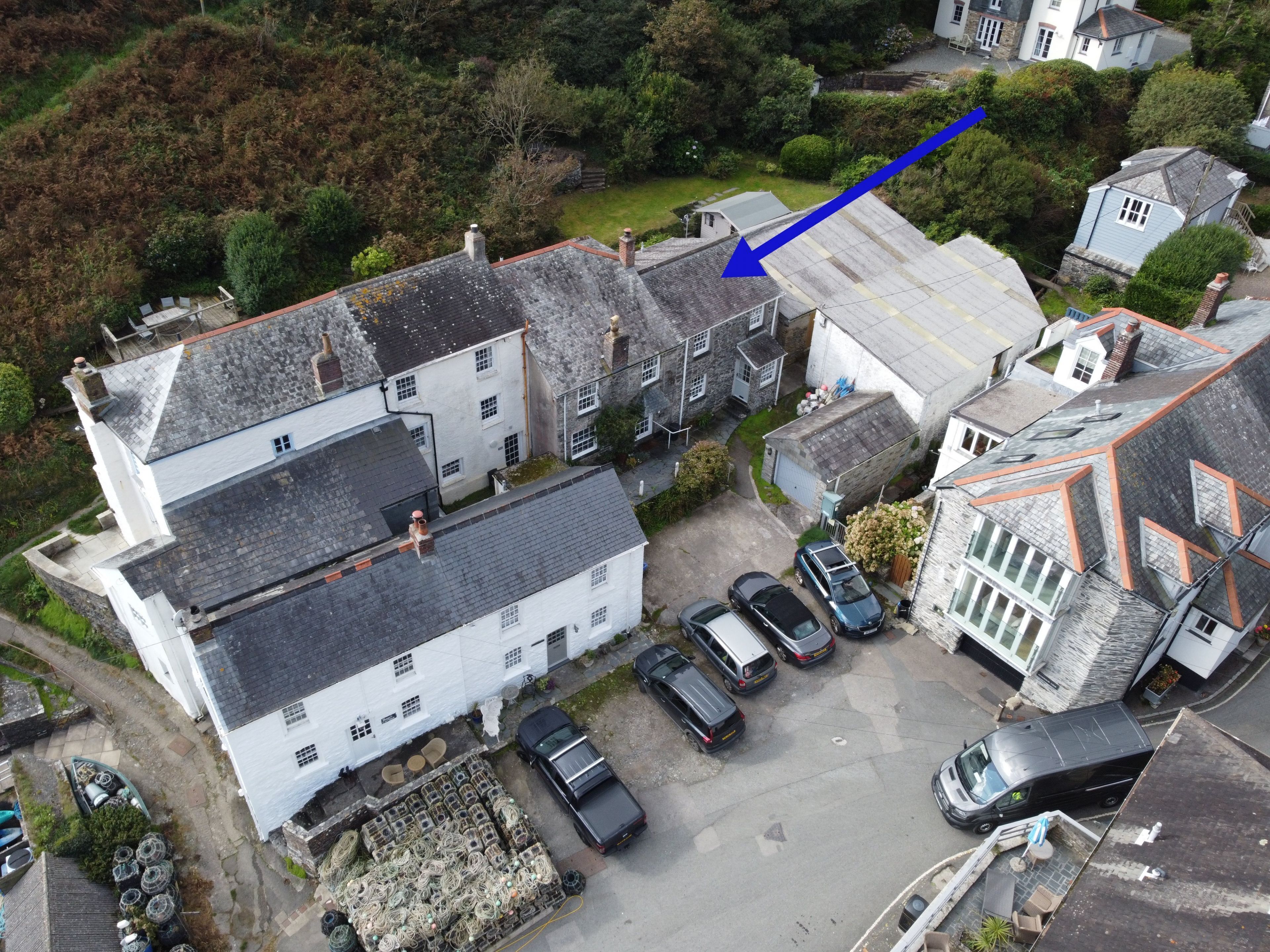 Vue aérienne d’un quartier résidentiel avec des maisons, des voitures garées et une grande pile de filets de pêche.