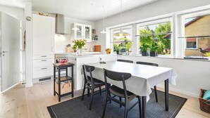 A modern kitchen with white cabinets, a dining table with chairs, and a view of the garden through large windows. - Awesome home in Nørre Nebel with WiFi (Nørre Nebel)