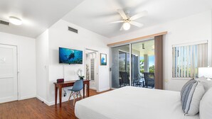 A hotel room with a large bed, a desk with a chair, a television, and a sliding glass door leading to an outdoor area.