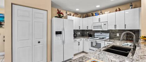 A modern kitchen with white cabinets, a granite countertop, a built-in oven, and a stainless steel sink.