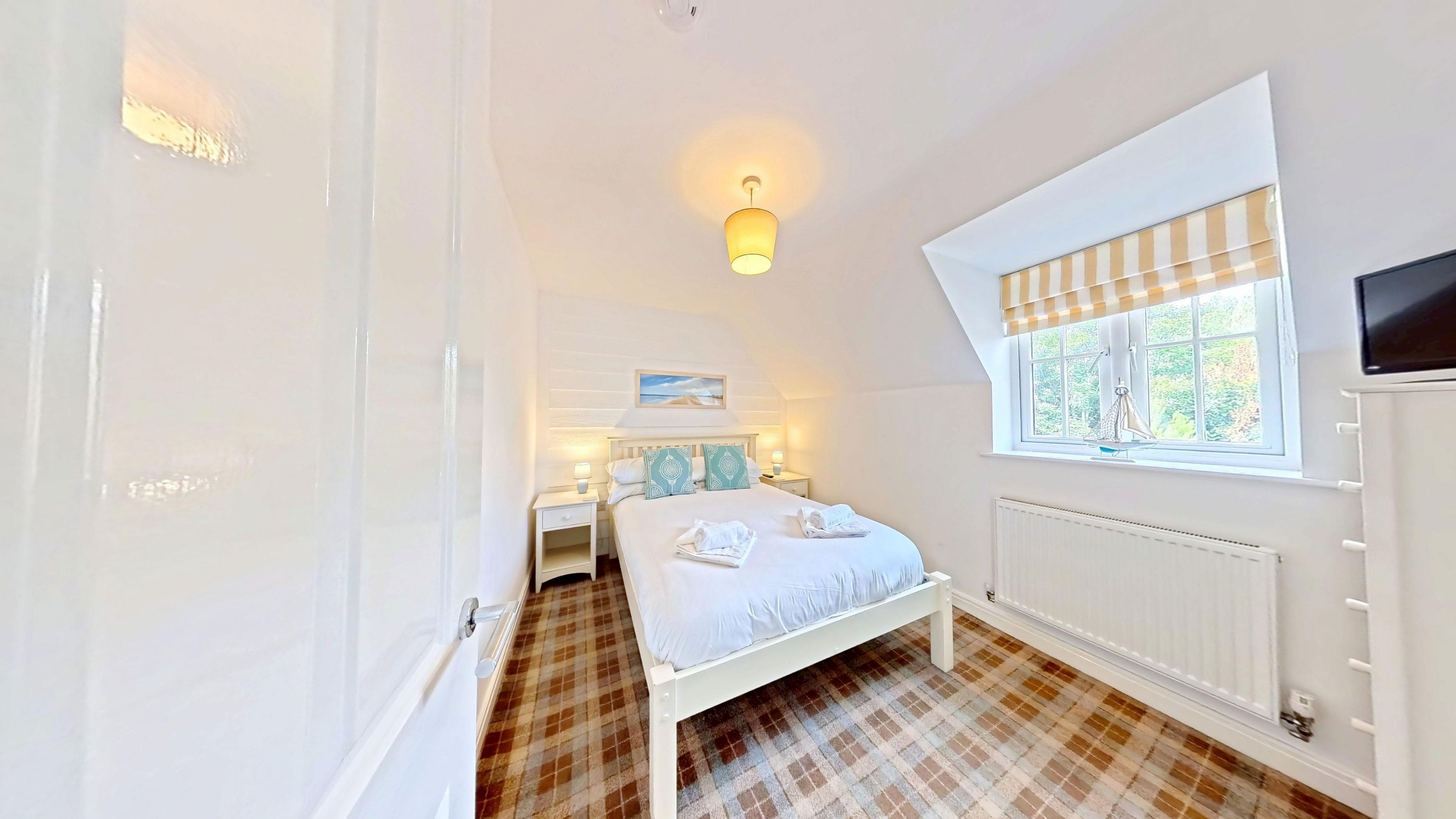 A bedroom with a bed, bedside tables, a window with blinds, a radiator, and a ceiling light.