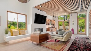 Un salon moderne doté d’un grand téléviseur, d’un plafond en bois et offrant une vue sur la verdure environnante.