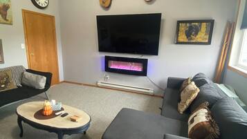 Una sala de estar con televisor de pantalla plana, dos guitarras, chimenea, sofá y mesa de centro.