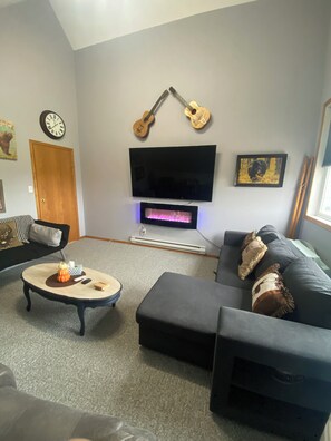 Una sala de estar con televisor de pantalla plana, dos guitarras, chimenea, sofá y mesa de centro.