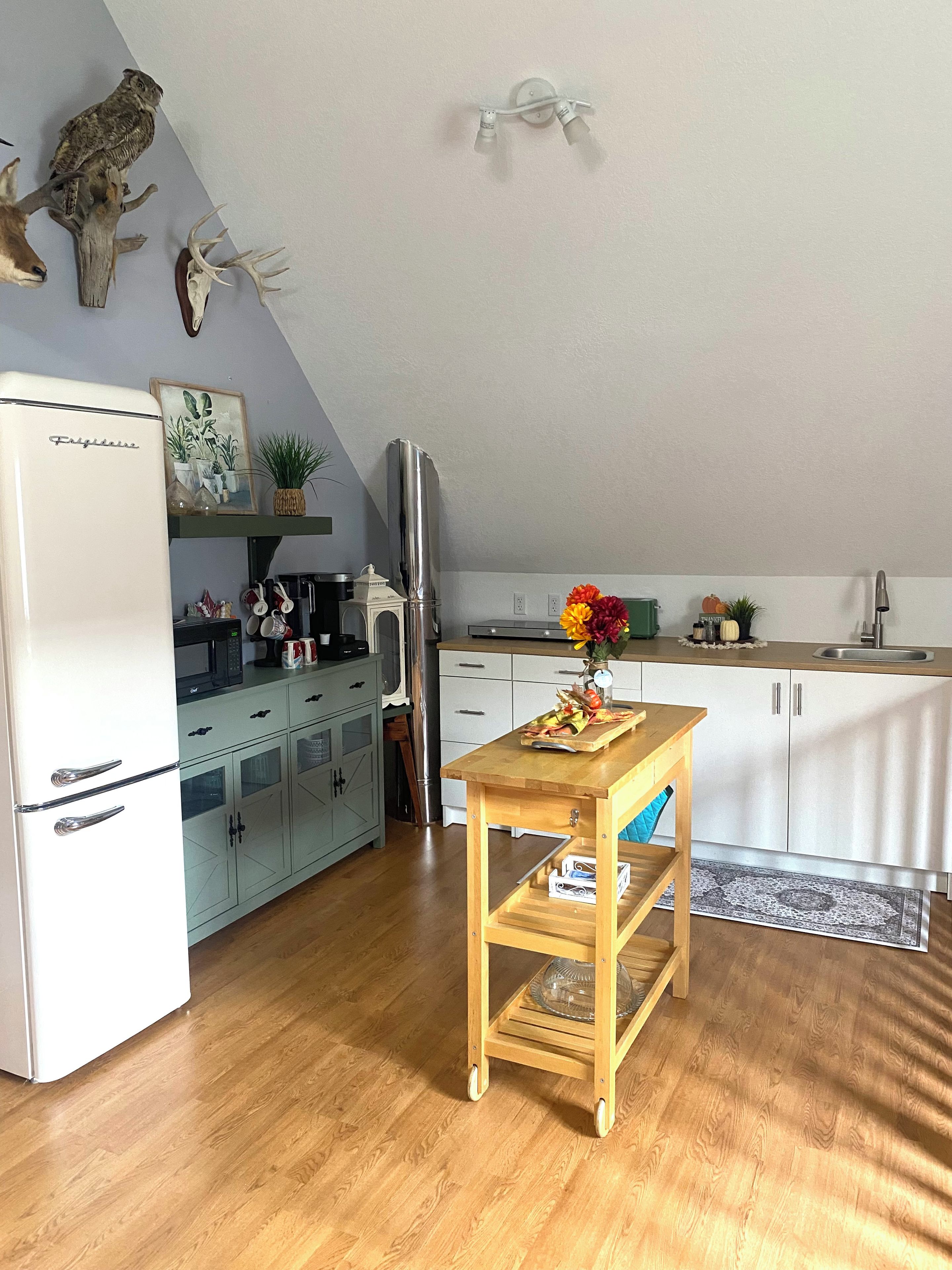 Cocina compacta con un refrigerador blanco, una mesa de madera con un florero y un microondas en la encimera.