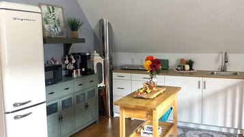 Cocina compacta con un refrigerador blanco, una mesa de madera con un florero y un microondas en la encimera.