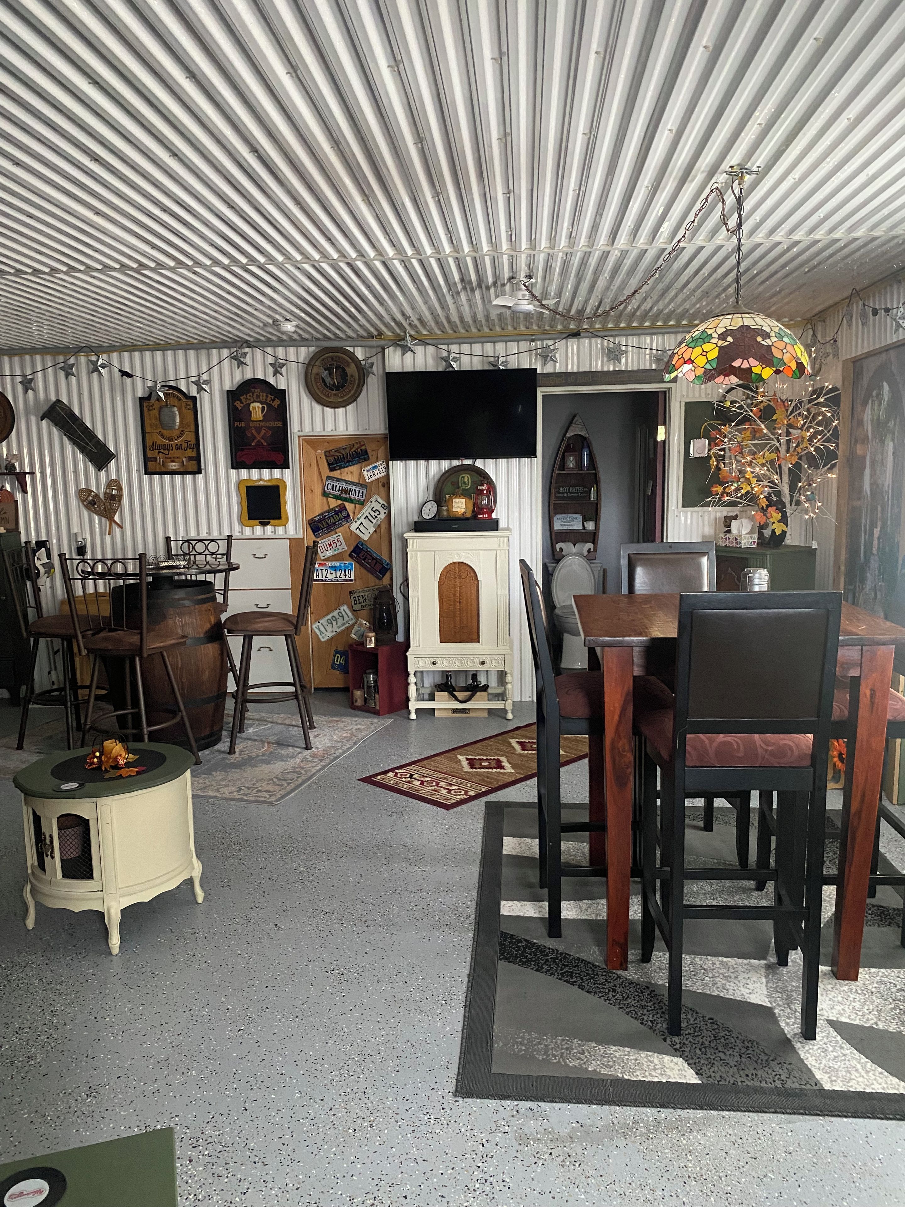 Spiseområde med bord og stole, et lille sofabord, en dekorativ lampe og et vægmonteret fjernsyn.