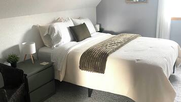 Un dormitorio con cama, mesitas de noche, lámpara, silla y una planta en la pared.