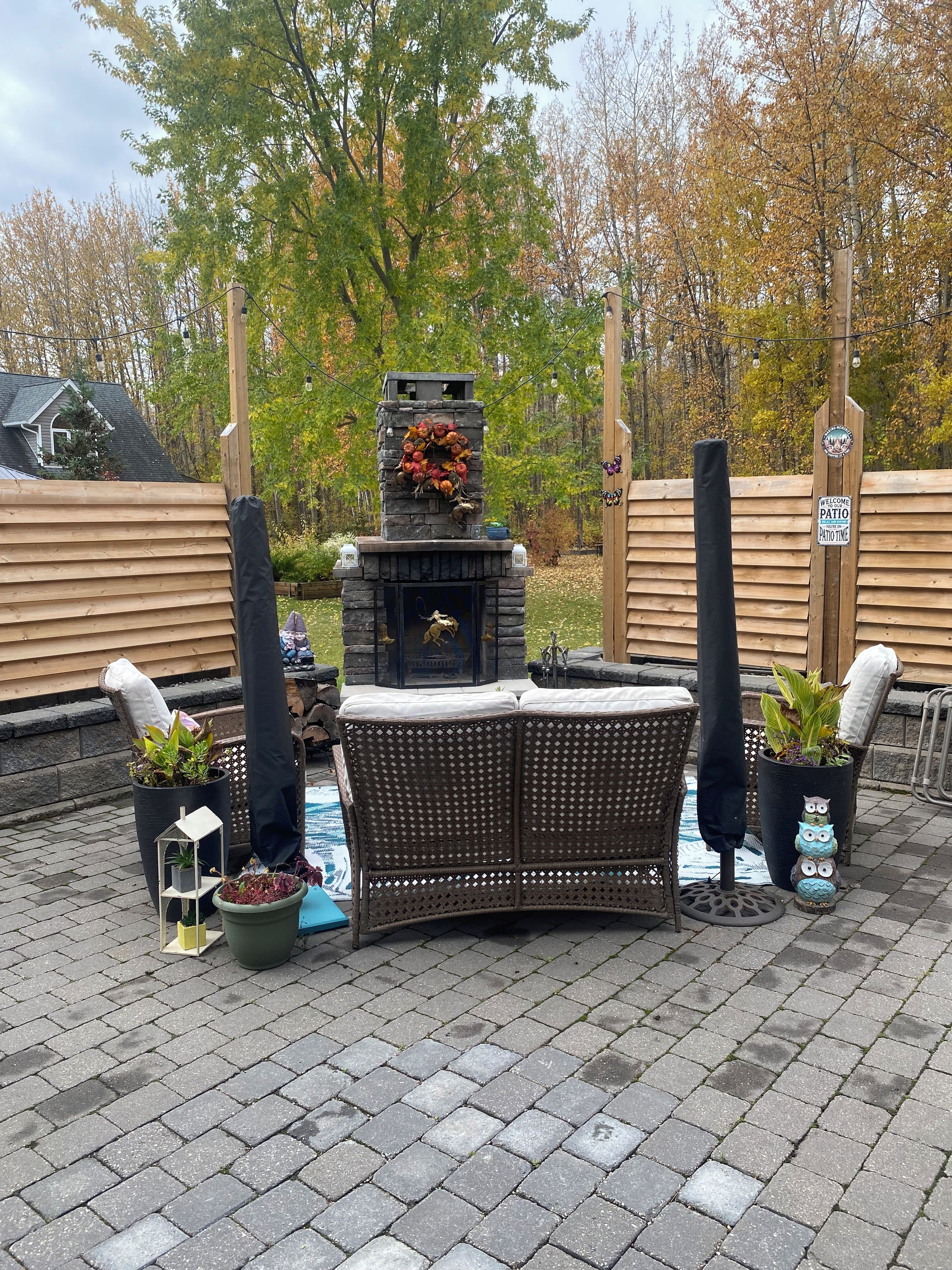 A patio area with a stone fireplace, wicker furniture, potted plants, and a 'Welcome Patio' sign.