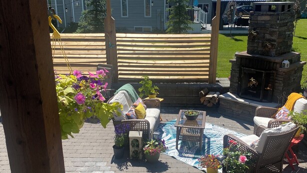 Un patio al aire libre con mobiliario de mimbre, plantas en macetas y una chimenea de piedra.