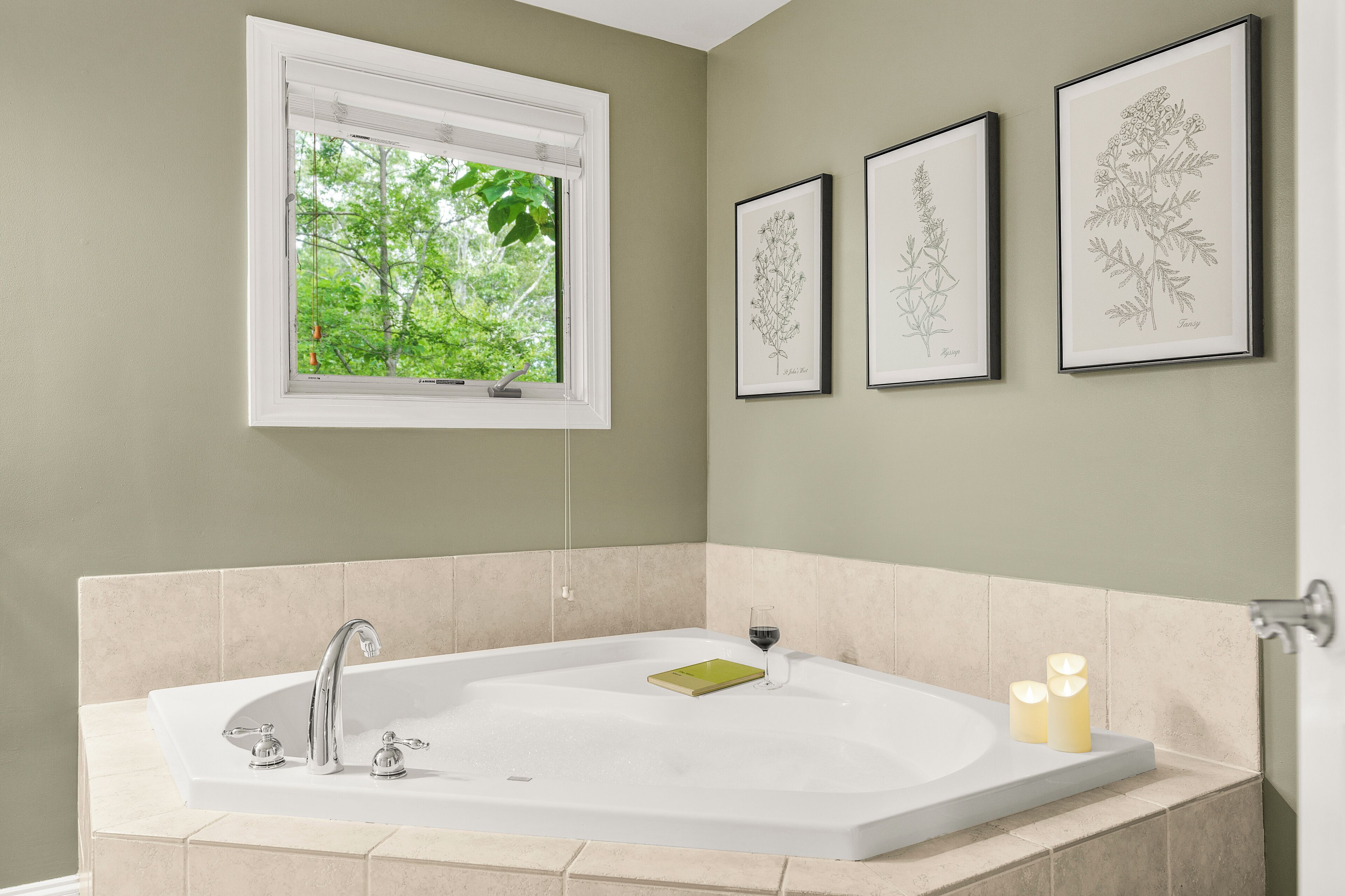 Une salle de bain avec une baignoire sur pieds, une fenêtre avec des stores et trois illustrations botaniques encadrées accrochées au mur.