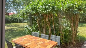 Eine Holzterrasse mit Tisch und Stühlen, umgeben von üppiger Bepflanzung und Bäumen.