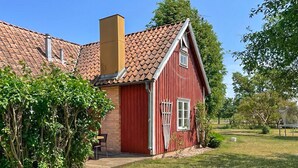 Ein rotes Holzhaus mit Ziegeldach, Schornstein und einer kleinen Veranda.
