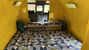 Un intérieur compact aux couleurs chaudes, avec un lit agrémenté d’une couvre-lit à motifs géométriques et de coussins assortis.