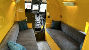 Un intérieur compact et jaune, avec deux canapés gris et des coussins turquoise, une petite table et une trousse de premiers secours visible.