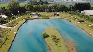 Une vue aérienne d’une vaste étendue d’eau rectangulaire, entourée de zones herbeuses et d’arbres, avec des bâtiments et des constructions à proximité.