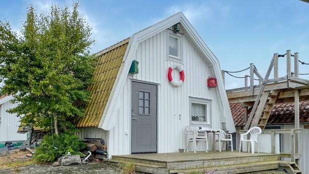 A white building with a grey door, a small porch with white plastic chairs, and a lifebuoy on the wall. - 1 bedroom cozy home in Vrångö (Vrångö)