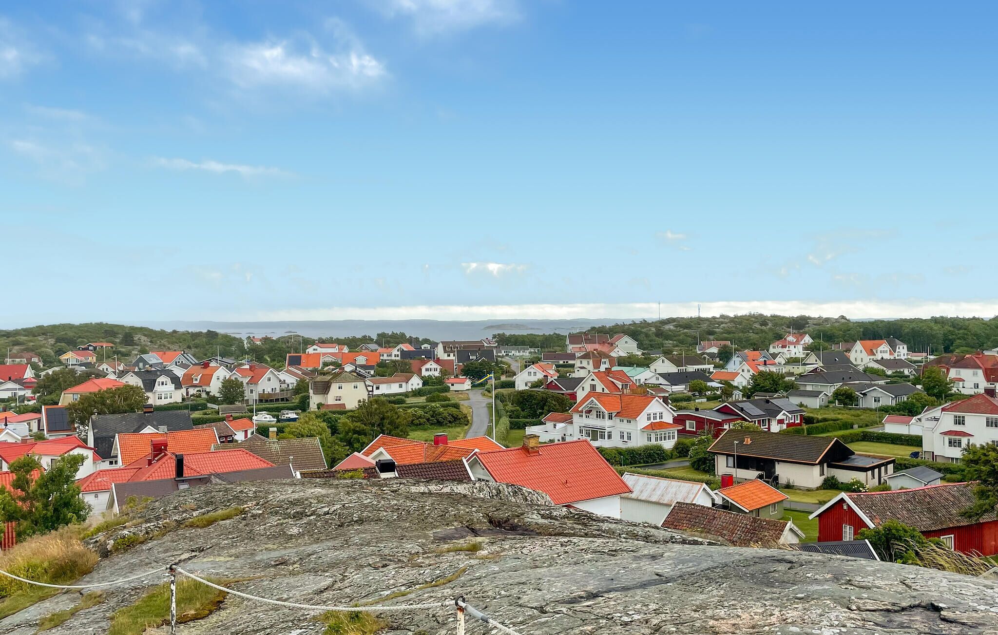 A coastal village with red-roofed houses, a rocky foreground, and a clear view of the sea and distant hills.