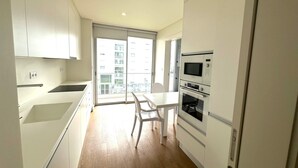 A modern kitchen with white cabinets, a dining table, and a large window. - Azores Paim Apartment T2 21A (Ponta Delgada)