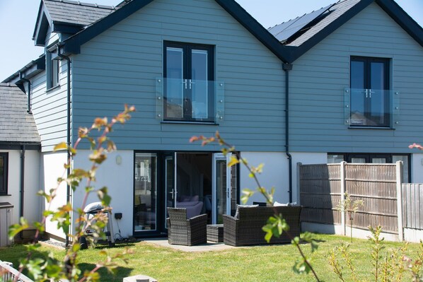 A two-story house with a sliding glass door leading to a patio area with outdoor furniture. - 5 Parc Delfryn - sleeps 7 guests in 3 bedrooms (Benllech)