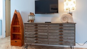 Une commode en bois avec de nombreux tiroirs, un téléviseur à écran plat fixé au mur, une lampe décorative et une étagère en bois.