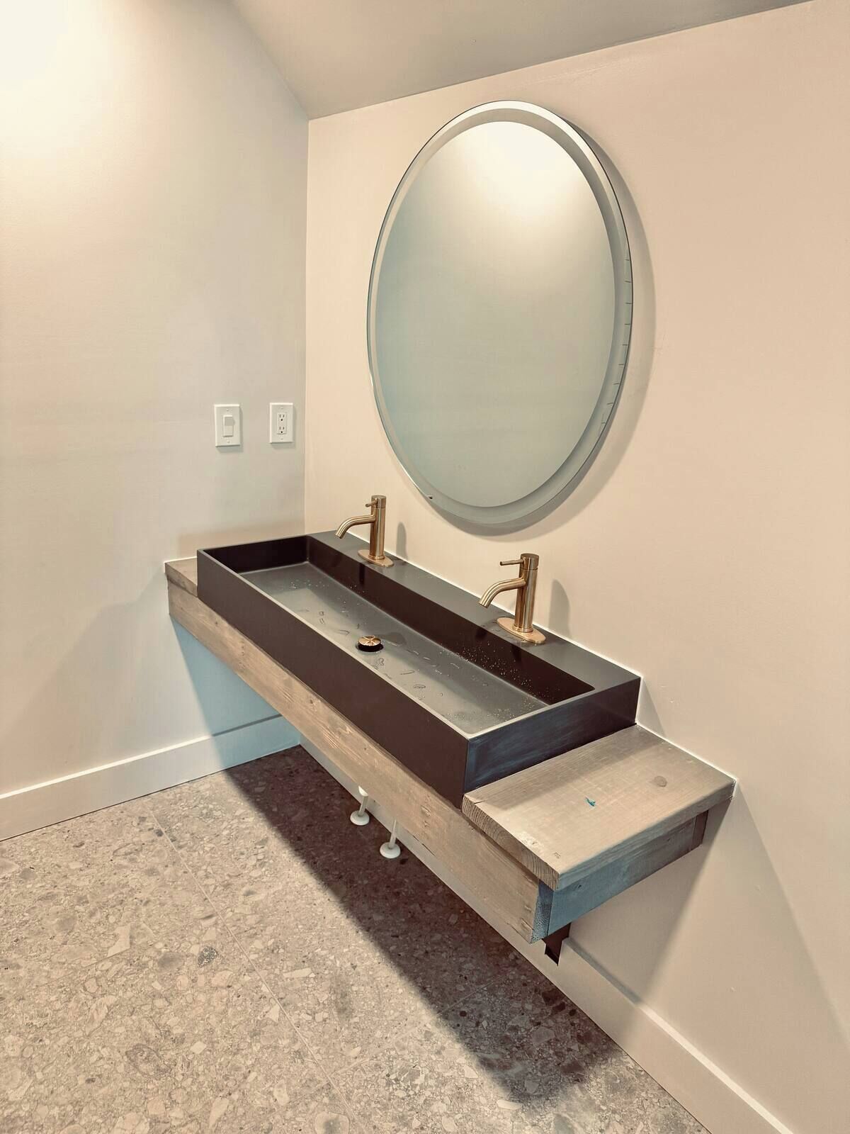 A modern bathroom with a rectangular sink, a round mirror, and a wooden vanity.