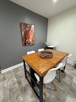 A dining area with a wooden table, white chairs, a woven basket, and a horse painting on the wall.