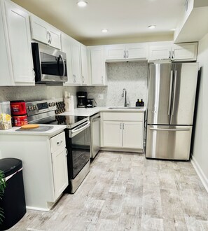 A modern kitchen with white cabinets, stainless steel appliances, and a marble backsplash.