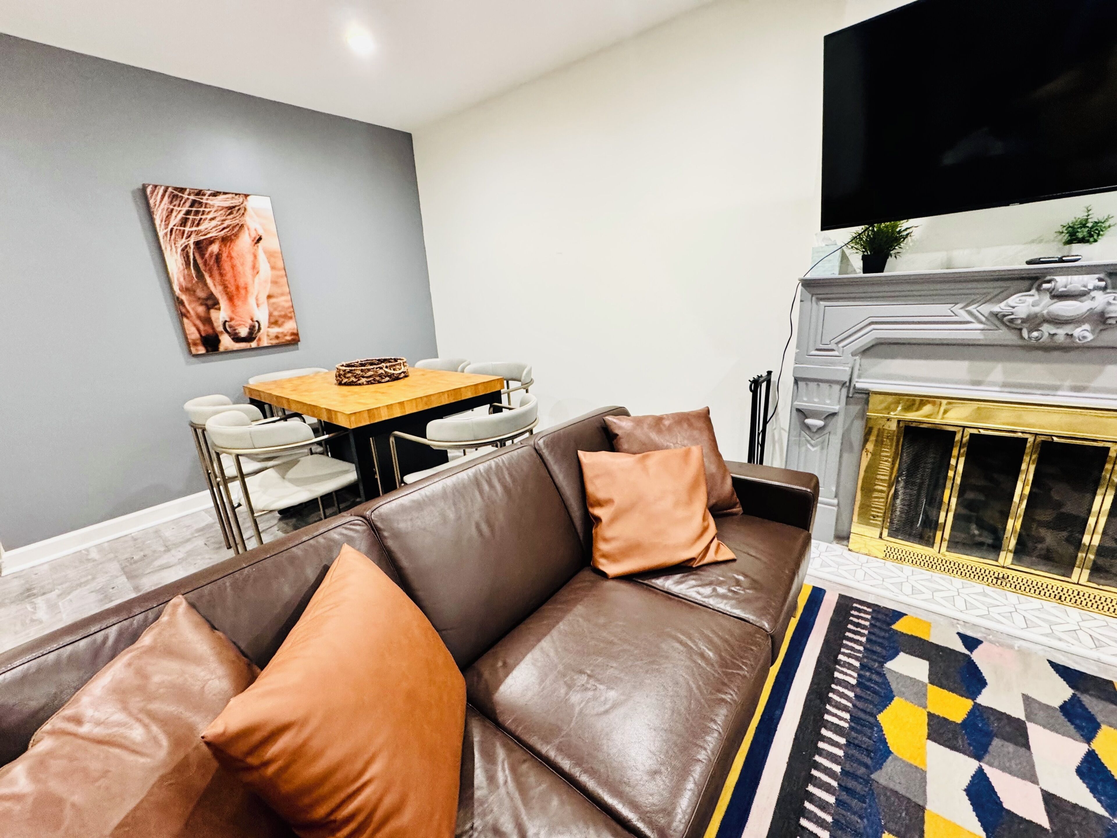 Een woonkamer met een bruine leren bank, een eettafel met stoelen, een open haard en een flatscreen televisie aan de muur.