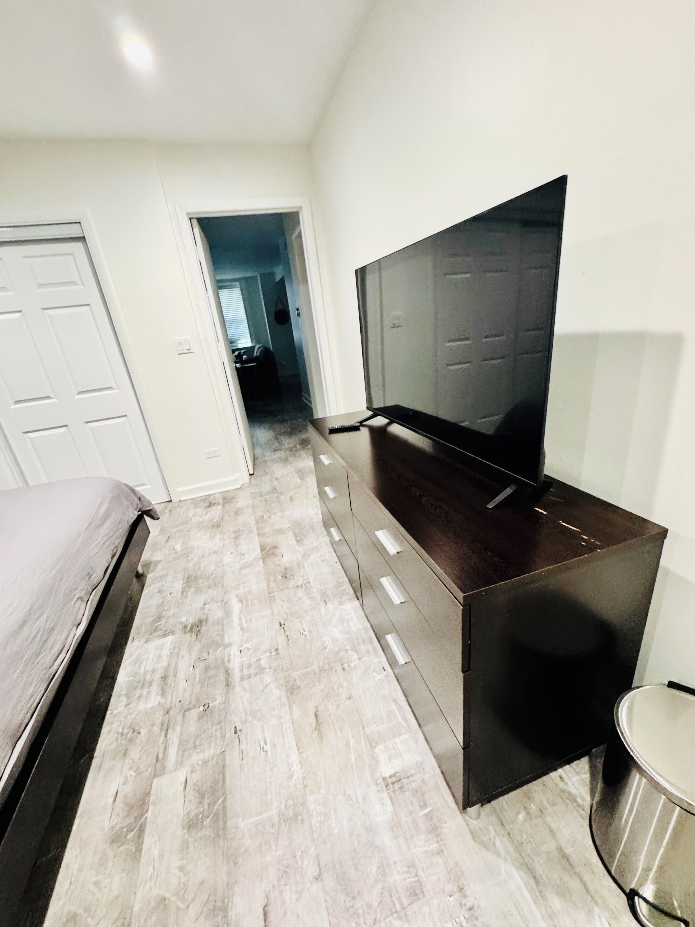 A bedroom with a bed, a TV on a stand, a small round table, and a door leading to another room.