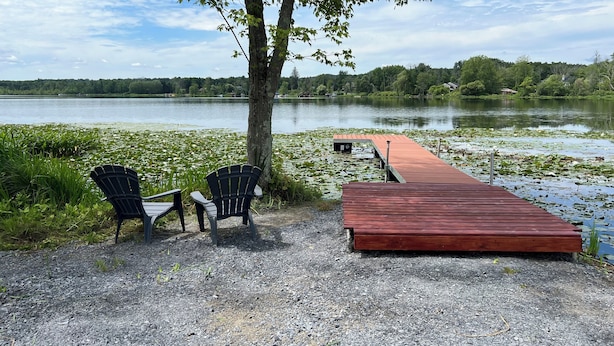Un quai en gravier qui s’avance dans un lac, avec deux chaises Adirondack et un petit abri de jardin.