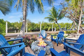 Une terrasse dotée de chaises Adirondack bleues, d’un foyer extérieur et offrant une vue sur un plan d’eau et la verdure environnante.