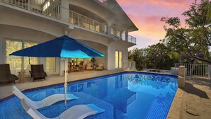 A swimming pool with lounge chairs and a patio area, surrounded by a two-story building with balconies. - Reel Joy | Florida Keys Waterfront Home + Pool & Private Dock (Marathon)