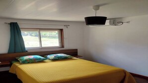 Ein Schlafzimmer mit einem Bett, einem Fenster mit Vorhängen, einem Nachttisch und einer Wandleuchte.