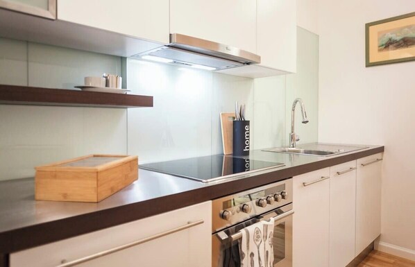 Una cocina moderna con armarios blancos, una campana extractora de acero inoxidable, una tabla de cortar de madera y un bloque de cuchillos negro.