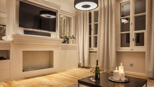 Una sala de estar moderna con chimenea, un televisor de pantalla plana montado encima y una mesa de comedor con velas y vasos.