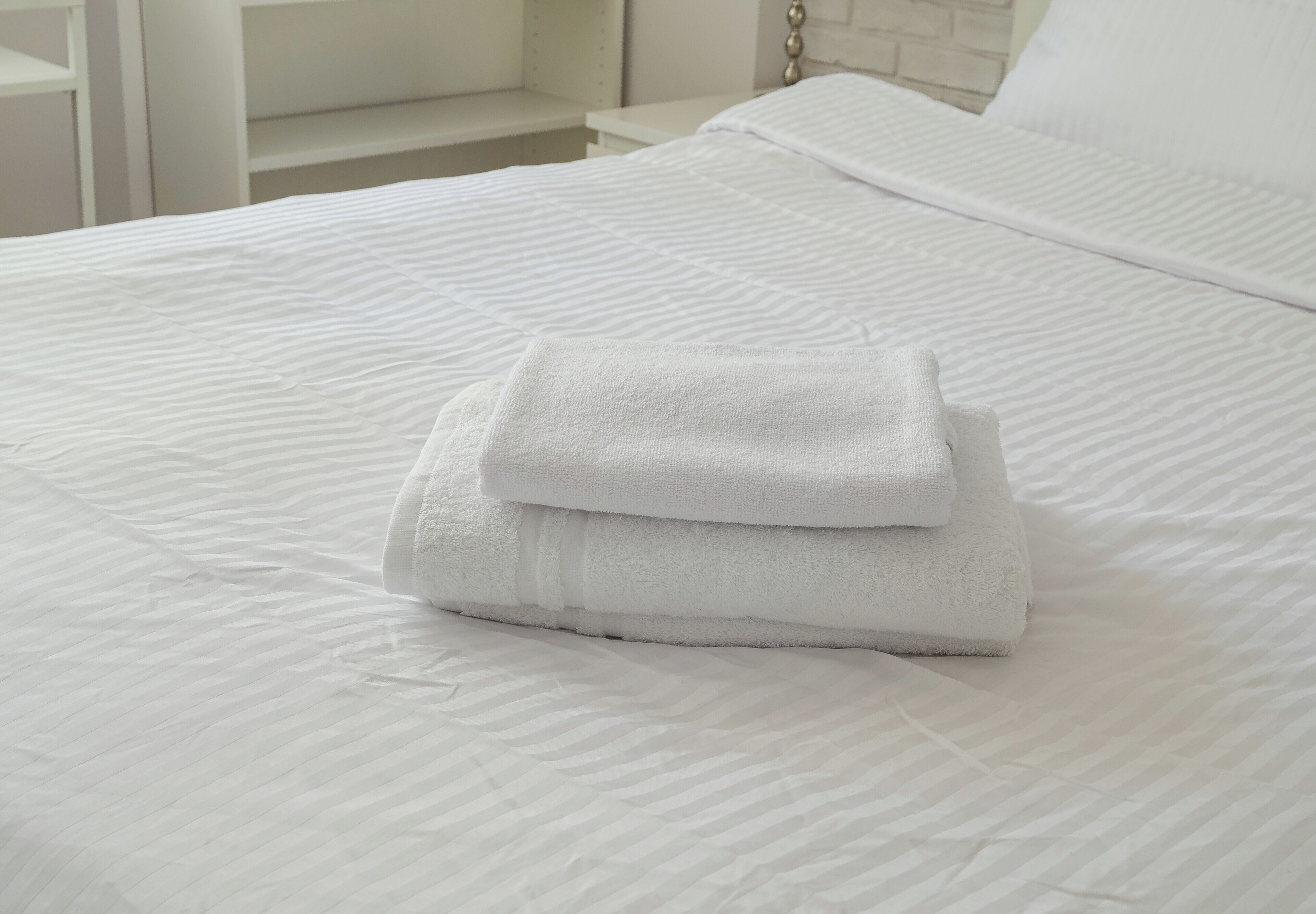 Una cama bien hecha con sábanas blancas y una toalla blanca doblada encima.